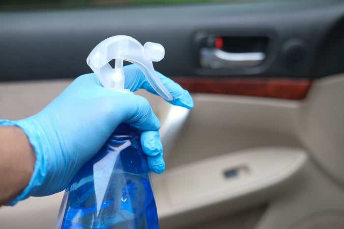 Hand in a blue glove holding a spray bottle inside a car
